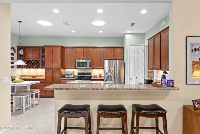 90 Canopy Glades Cir, Ponte Vedra, FL 32081 - kitchen with stainless steel appliances, a peninsula, brown cabinets, a kitchen breakfast bar, and light tile patterned floors