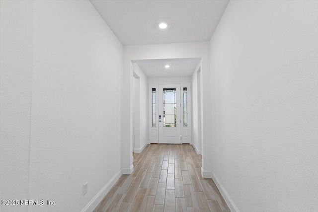 corridor with baseboards, light wood finished floors, and recessed lighting