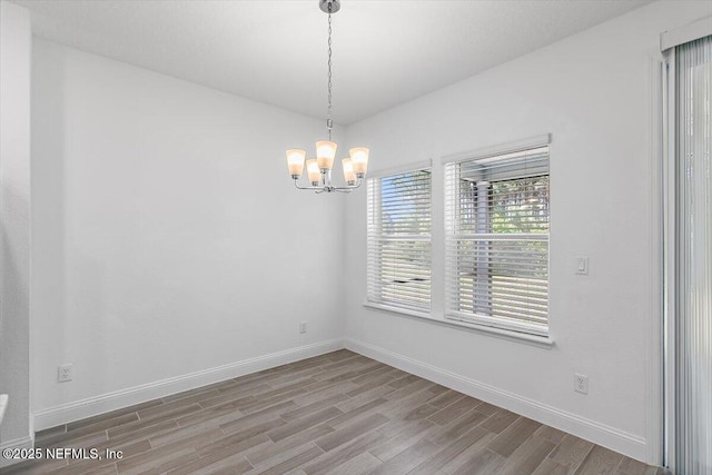unfurnished room with an inviting chandelier, wood finished floors, and baseboards