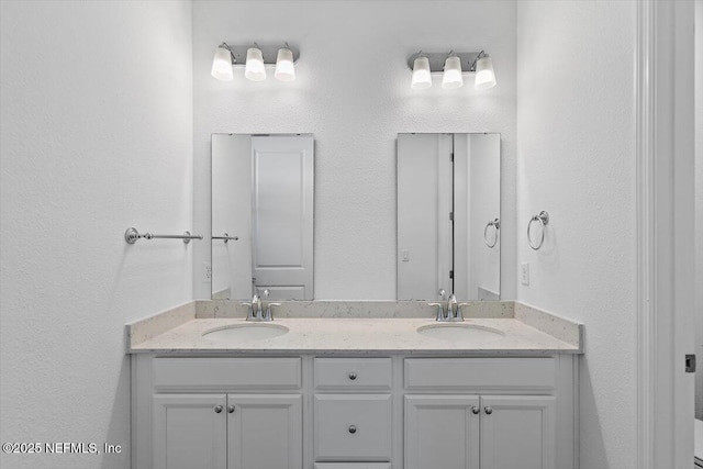 full bath featuring a sink, double vanity, and a textured wall
