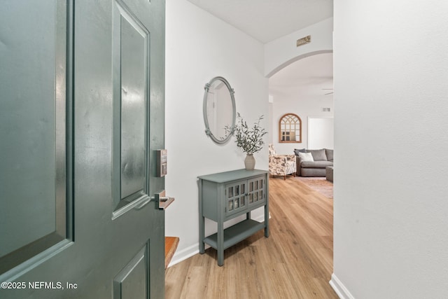 foyer with arched walkways, light wood-style flooring, and baseboards