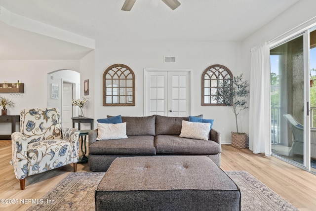 living area featuring arched walkways, light wood finished floors, and a ceiling fan