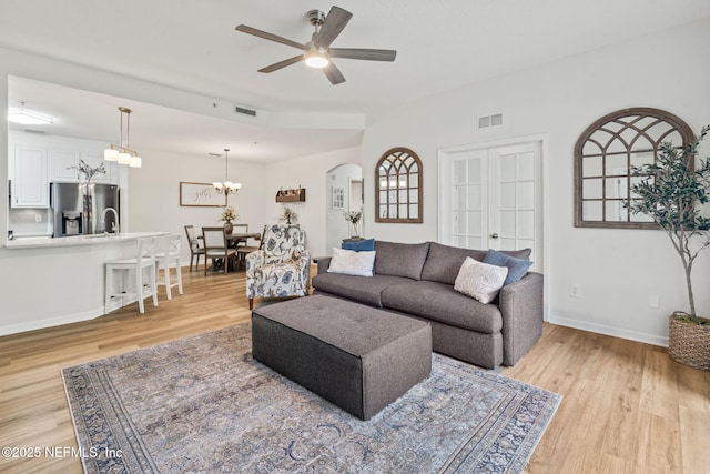 living area featuring light wood finished floors, arched walkways, baseboards, ceiling fan, and a chandelier