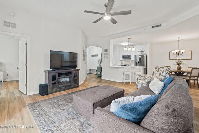 living room with a ceiling fan, arched walkways, light wood finished floors, a chandelier, and baseboards
