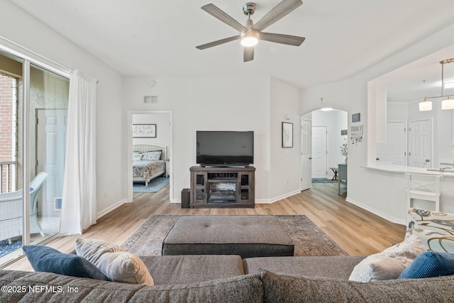 living area with a ceiling fan, wood finished floors, arched walkways, and baseboards
