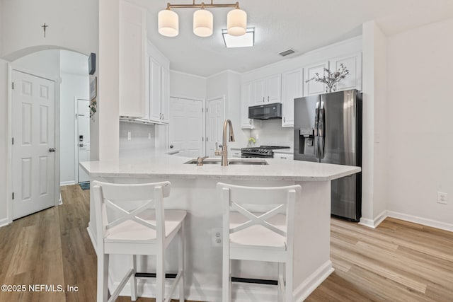 kitchen with appliances with stainless steel finishes, a sink, light wood-style floors, white cabinets, and a kitchen breakfast bar