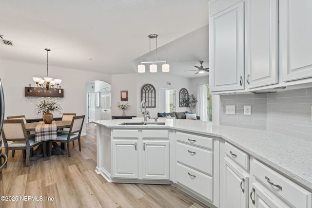 kitchen featuring a sink, arched walkways, ceiling fan, tasteful backsplash, and white cabinetry
