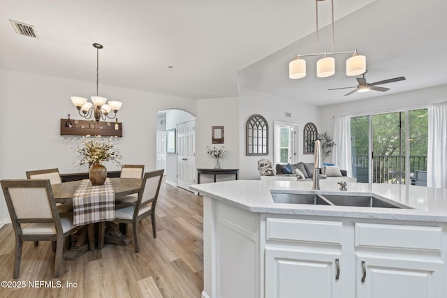 kitchen with a sink, arched walkways, light wood-type flooring, white cabinetry, and a chandelier