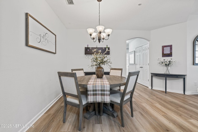 dining room featuring light wood-style floors, arched walkways, a chandelier, and baseboards