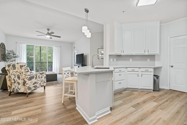 kitchen featuring a sink, a peninsula, light wood-type flooring, white cabinets, and open floor plan