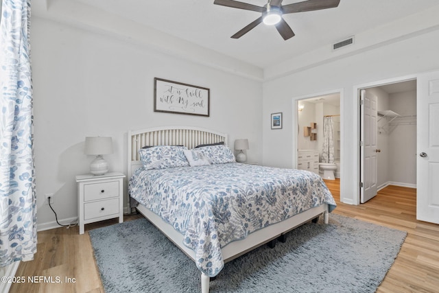 bedroom with wood finished floors, ensuite bath, a ceiling fan, baseboards, and a spacious closet