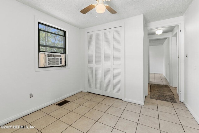 unfurnished bedroom with light tile patterned floors, a textured ceiling, a closet, baseboards, and a ceiling fan
