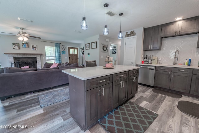 kitchen with stainless steel dishwasher, a sink, light wood finished floors, a ceiling fan, and light countertops