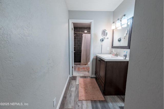 full bathroom featuring wood finished floors, tiled shower, toilet, vanity, and baseboards