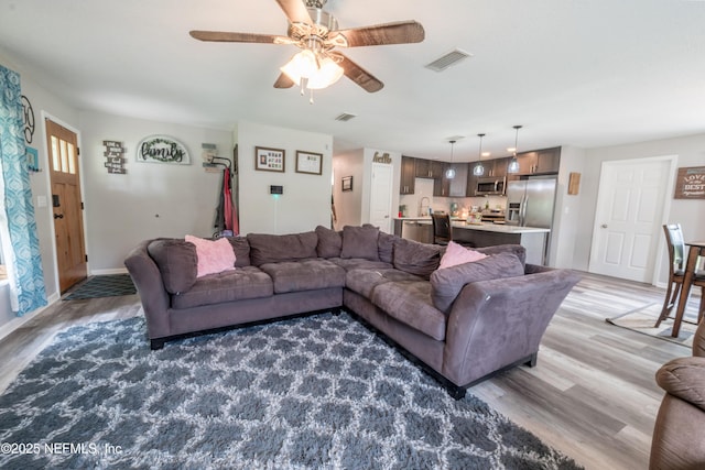 living area featuring light wood finished floors, a ceiling fan, and baseboards