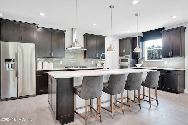 kitchen with appliances with stainless steel finishes, a sink, wall chimney range hood, decorative backsplash, and a breakfast bar