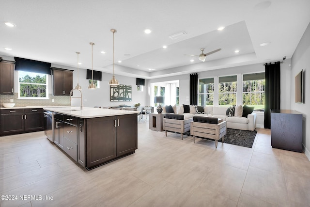kitchen featuring a sink, dark brown cabinetry, a tray ceiling, light countertops, and open floor plan