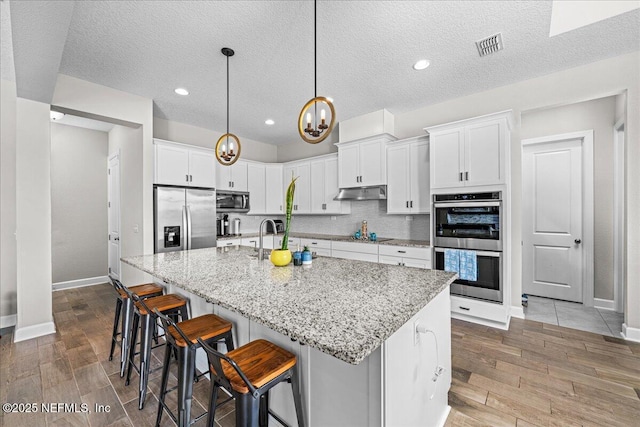 71 Lansing Ct, Saint Augustine, FL 32092 - kitchen with stainless steel appliances, under cabinet range hood, white cabinets, baseboards, and a textured ceiling