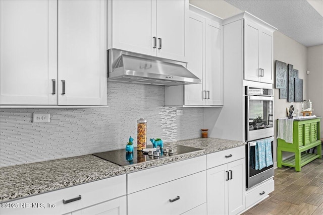 71 Lansing Ct, Saint Augustine, FL 32092 - kitchen with black electric cooktop, under cabinet range hood, double oven, light stone countertops, and white cabinetry