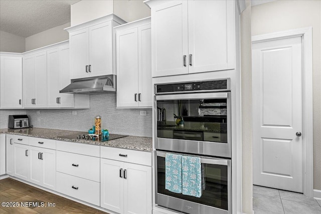 71 Lansing Ct, Saint Augustine, FL 32092 - kitchen with stainless steel double oven, under cabinet range hood, light stone counters, black electric stovetop, and white cabinetry