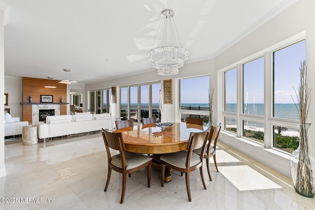 dining room featuring a chandelier, a glass covered fireplace, ornamental molding, and a water view