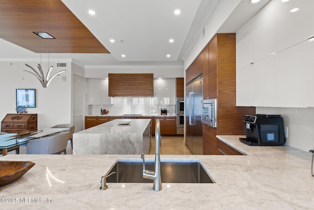 kitchen with modern cabinets, brown cabinets, a sink, stainless steel appliances, and crown molding