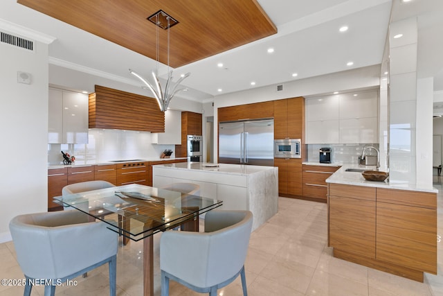 kitchen featuring modern cabinets, built in appliances, a sink, brown cabinets, and backsplash
