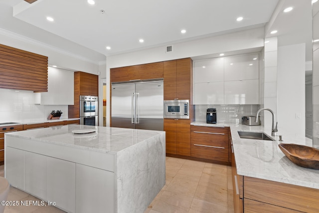 kitchen with built in appliances, modern cabinets, a sink, decorative backsplash, and ornamental molding