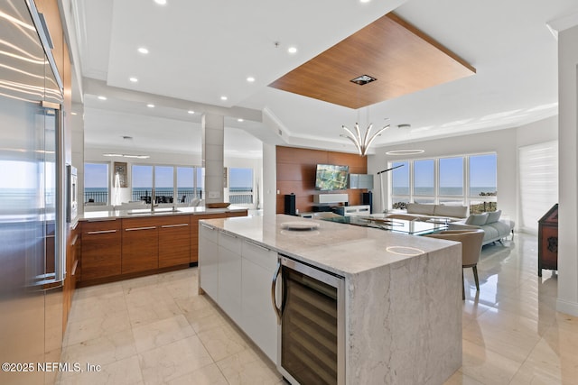 kitchen with beverage cooler, a raised ceiling, modern cabinets, open floor plan, and brown cabinets