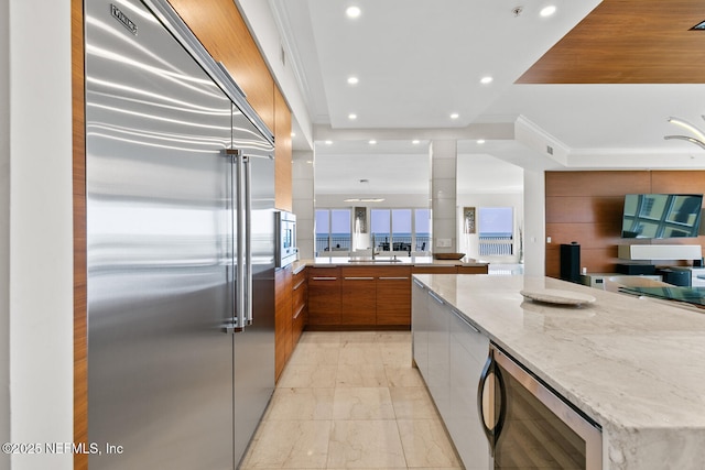 kitchen with built in appliances, modern cabinets, open floor plan, brown cabinetry, and a sink