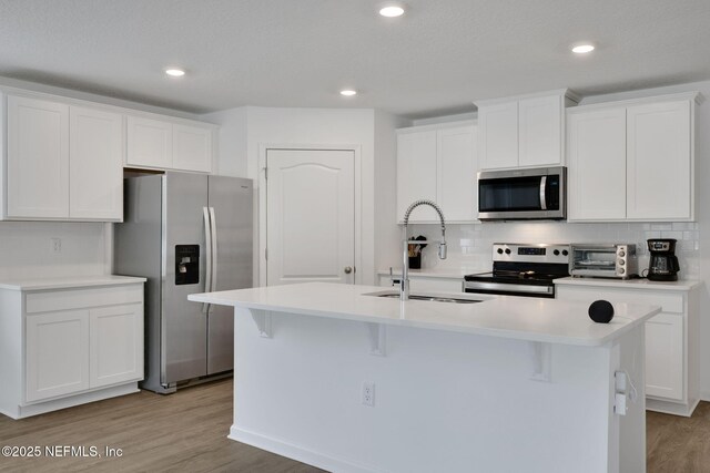 2304 Shady Breeze Ln, Green Cove Springs, FL 32043 - kitchen with stainless steel appliances, a sink, light wood-type flooring, a kitchen island with sink, and decorative backsplash