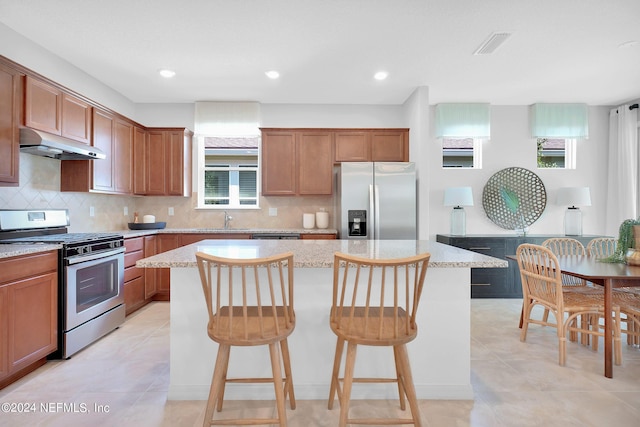 kitchen with stainless steel appliances, under cabinet range hood, a center island, a sink, and a breakfast bar