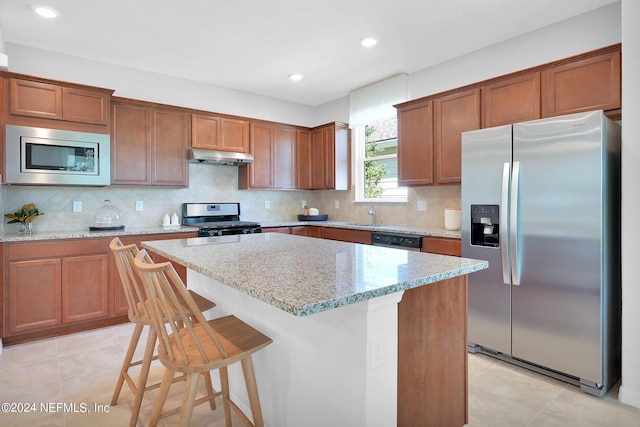 kitchen featuring appliances with stainless steel finishes, under cabinet range hood, light tile patterned floors, a kitchen island, and recessed lighting