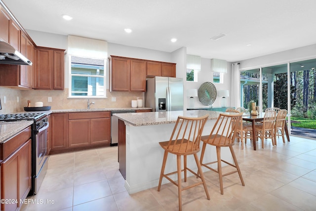 kitchen featuring stainless steel appliances, a sink, a kitchen island, decorative backsplash, and a kitchen bar