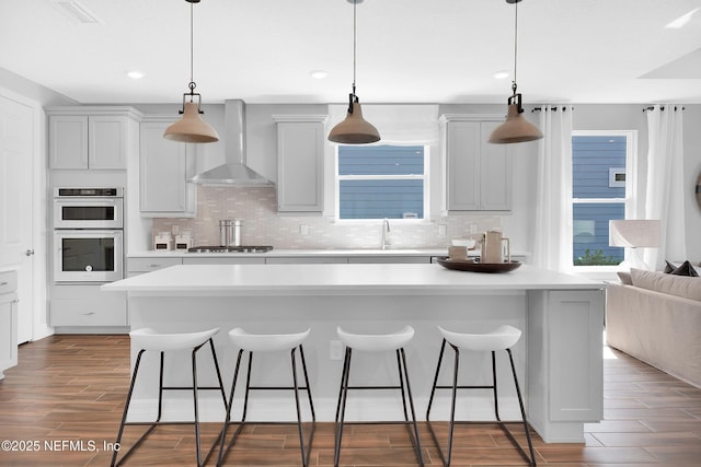 kitchen with wall chimney range hood, double oven, a breakfast bar area, tasteful backsplash, and recessed lighting