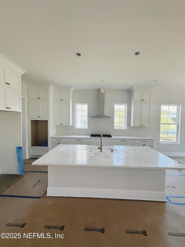 99 Sullivan Pl, Saint Johns, FL 32259 - kitchen featuring wall chimney range hood, a kitchen island with sink, white cabinets, light stone counters, and gas stovetop
