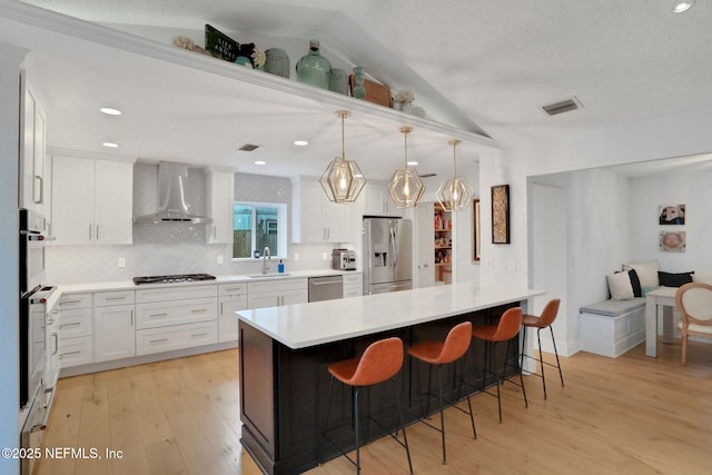 1257 12th St N, Jacksonville Beach, FL 32250 - kitchen with stainless steel appliances, wall chimney exhaust hood, a kitchen bar, backsplash, and light wood-style flooring