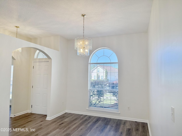 empty room with arched walkways, wood finished floors, baseboards, and a textured ceiling