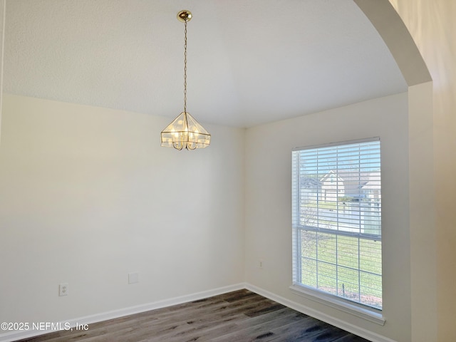 unfurnished room featuring healthy amount of natural light, arched walkways, dark wood-style flooring, a chandelier, and vaulted ceiling