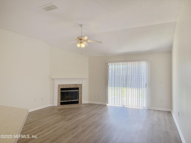 unfurnished living room with wood finished floors, a ceiling fan, a tiled fireplace, baseboards, and lofted ceiling