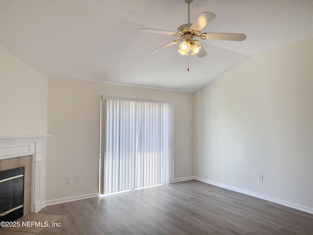 unfurnished living room with wood finished floors, ceiling fan, a tiled fireplace, a textured ceiling, and baseboards