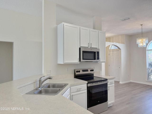 kitchen featuring appliances with stainless steel finishes, a sink, white cabinets, a chandelier, and light wood finished floors