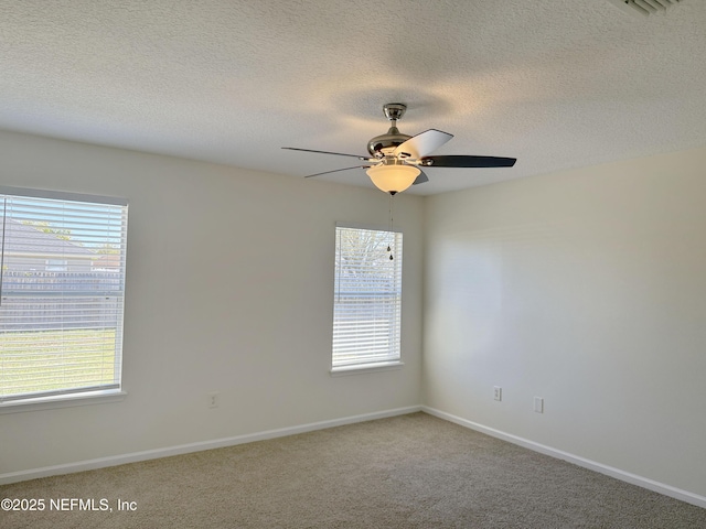 empty room with ceiling fan, healthy amount of natural light, a textured ceiling, carpet flooring, and baseboards