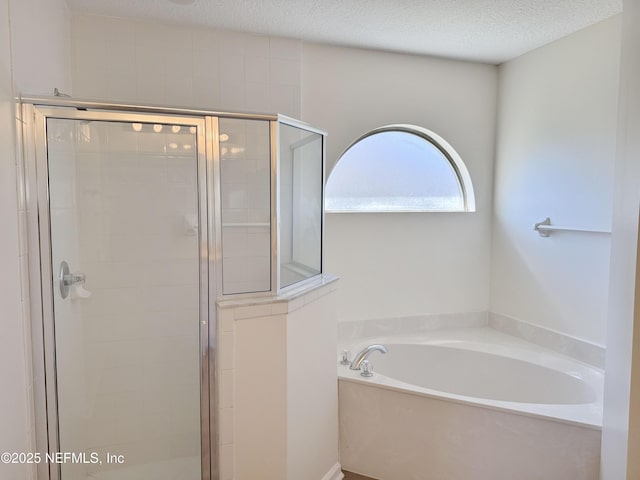 bathroom with a stall shower, a bath, and a textured ceiling