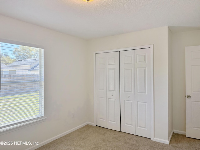 unfurnished bedroom featuring light carpet, a closet, baseboards, and a textured ceiling