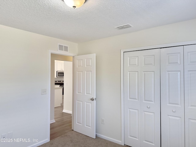 unfurnished bedroom featuring a closet, a textured ceiling, baseboards, and light carpet