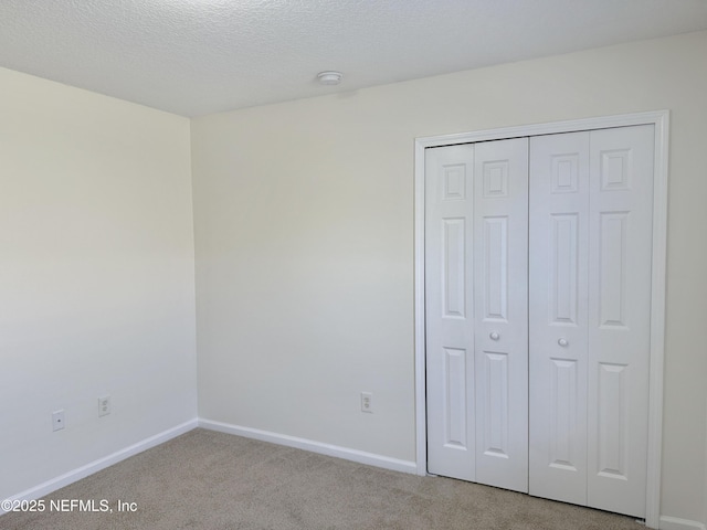 unfurnished bedroom featuring carpet, baseboards, a closet, and a textured ceiling