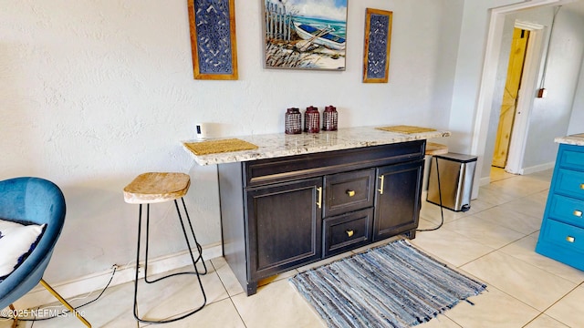 indoor dry bar with light tile patterned flooring and baseboards