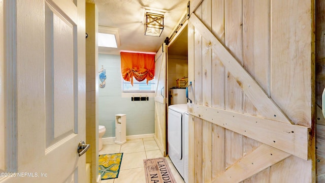 laundry room with light tile patterned floors, water heater, and a barn door
