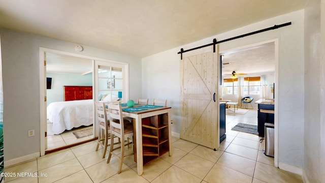 dining area with a barn door, a ceiling fan, light tile patterned floors, and baseboards